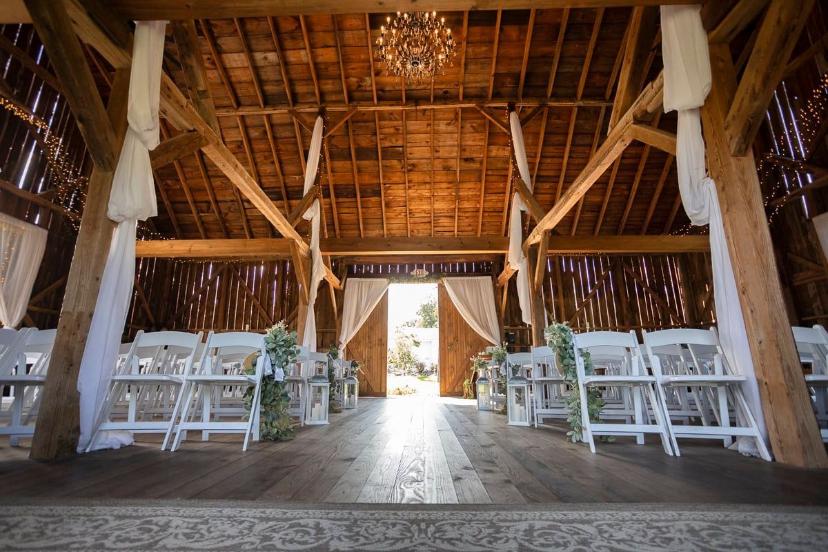The inside of a barn decorated for a wedding ceremony with white chairs.