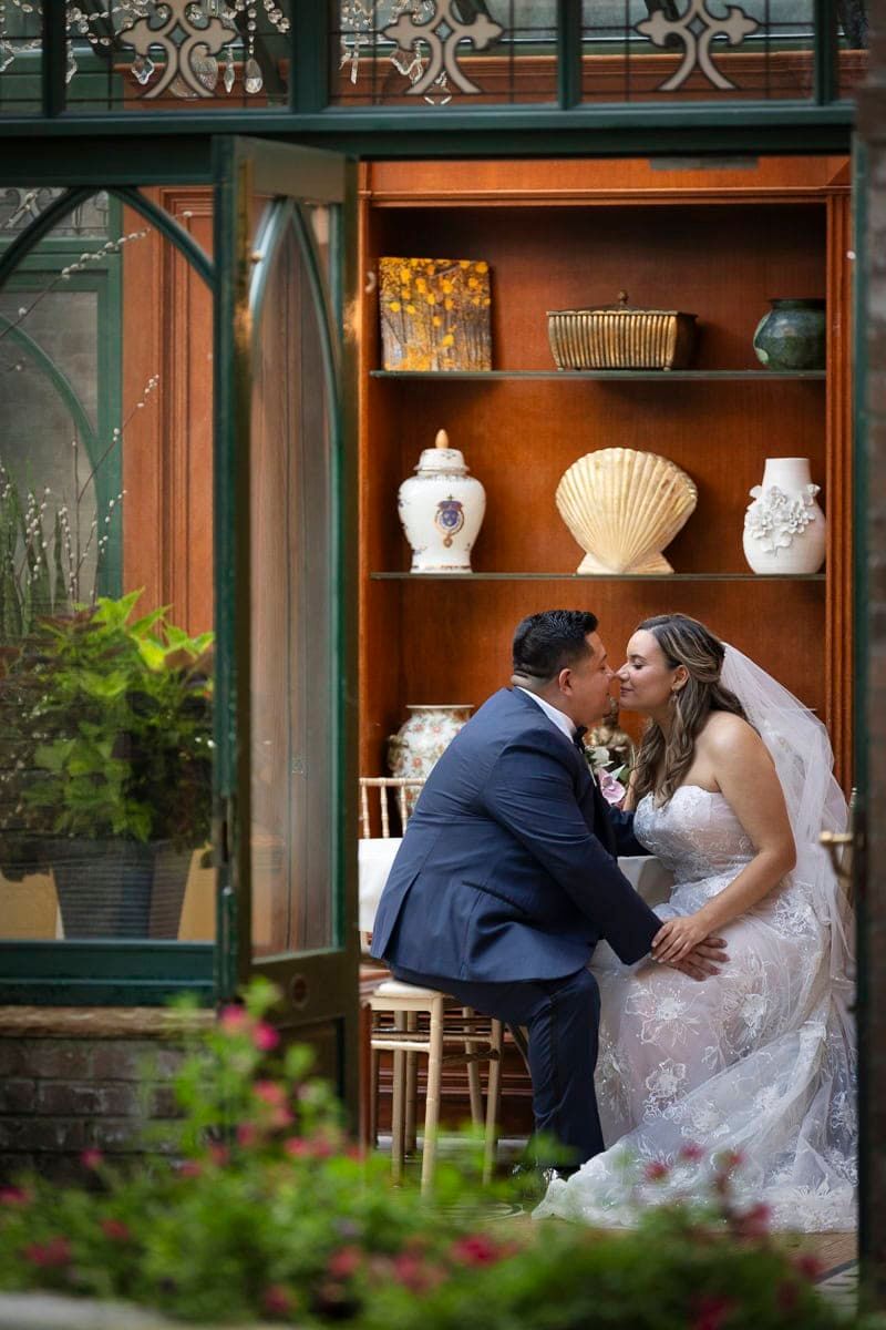 A bride and groom are kissing in a greenhouse.