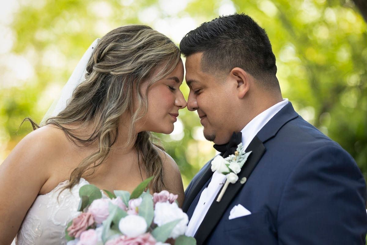 A bride and groom are kissing each other on the forehead.