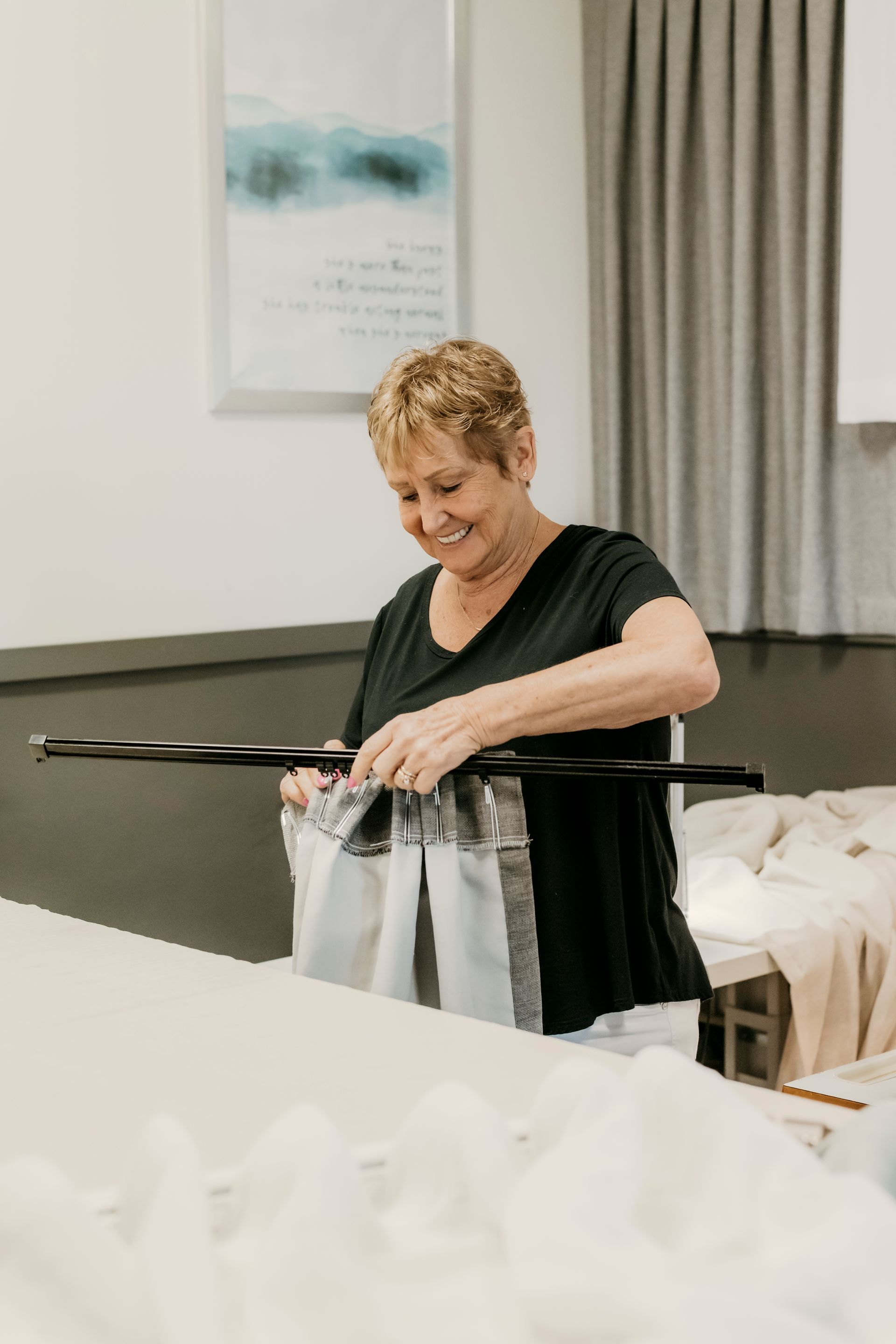Person packing clothing into a suitcase in a bright room, smiling beside a bed and curtains — Curtain Concepts in Dunbible, NSW