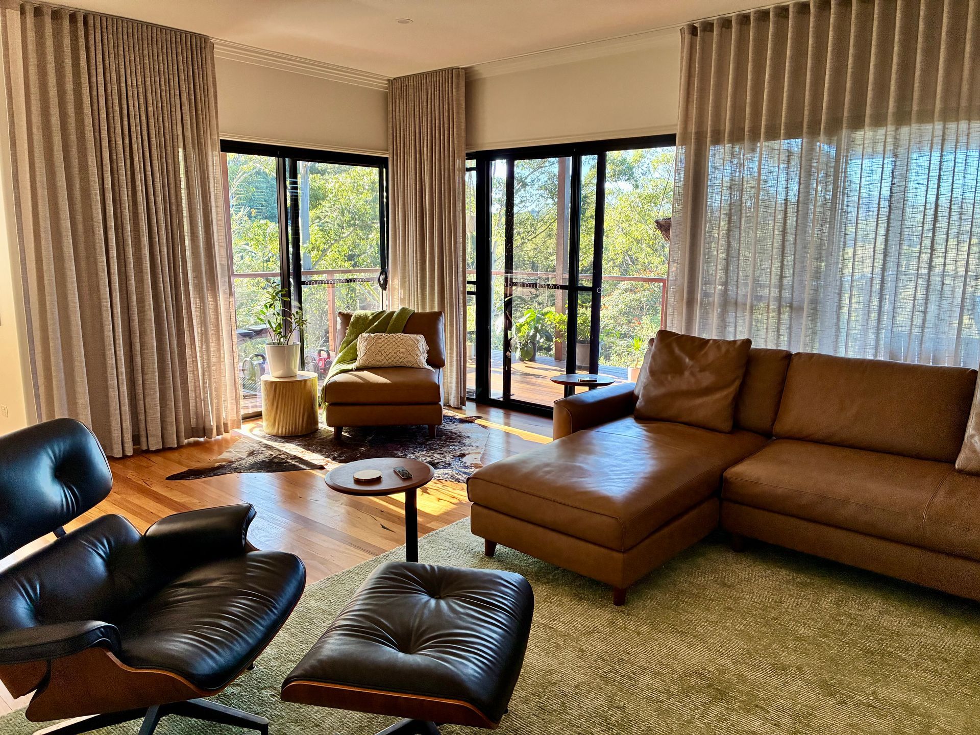 Modern living room with tan sectional, black lounge chair, ottoman, large windows, and sheer curtains— Curtain Concepts in Dunbible, NSW