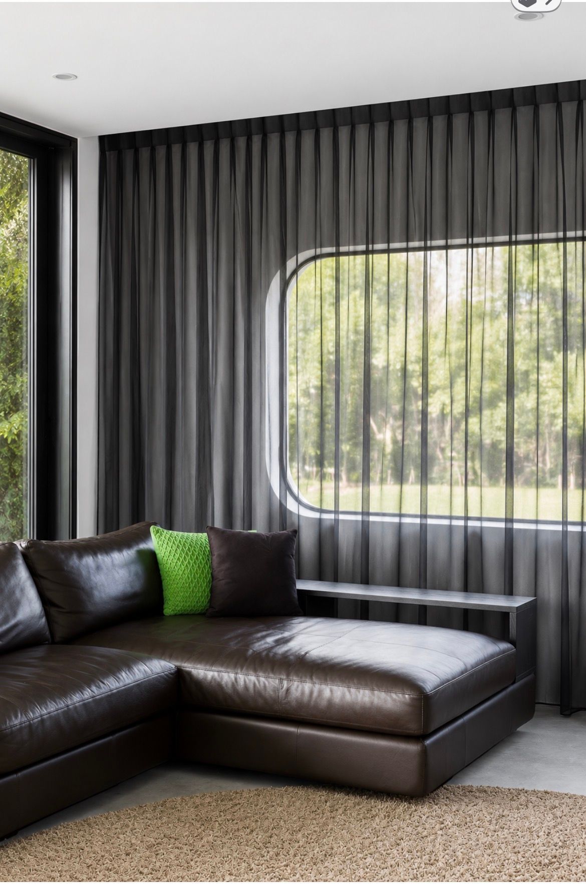 Modern living room with dark leather sectional, gray curtains, and large rounded window letting in daylight — Curtain Concepts in Dunbible, NSW