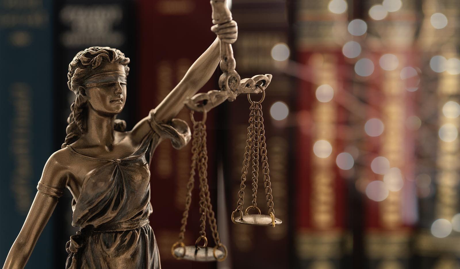 A statue of lady justice holding scales of justice in front of a row of books.