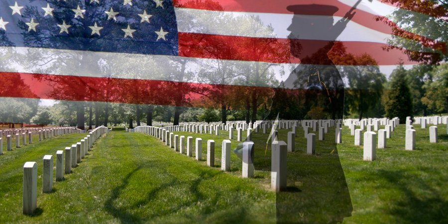 A soldier is standing in front of a cemetery with an american flag in the background.