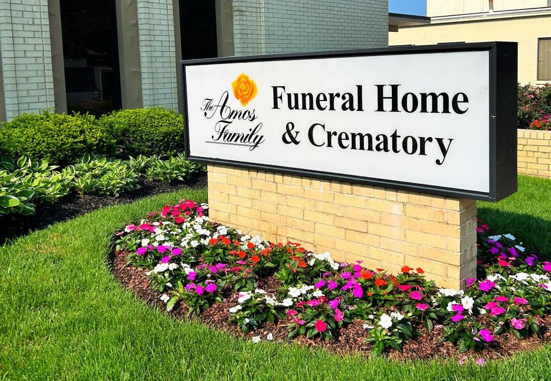 A funeral home and crematory sign with flowers in front of it.