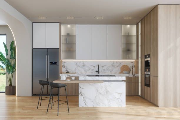 A kitchen with a marble counter top , stools , a refrigerator , and a sink.
