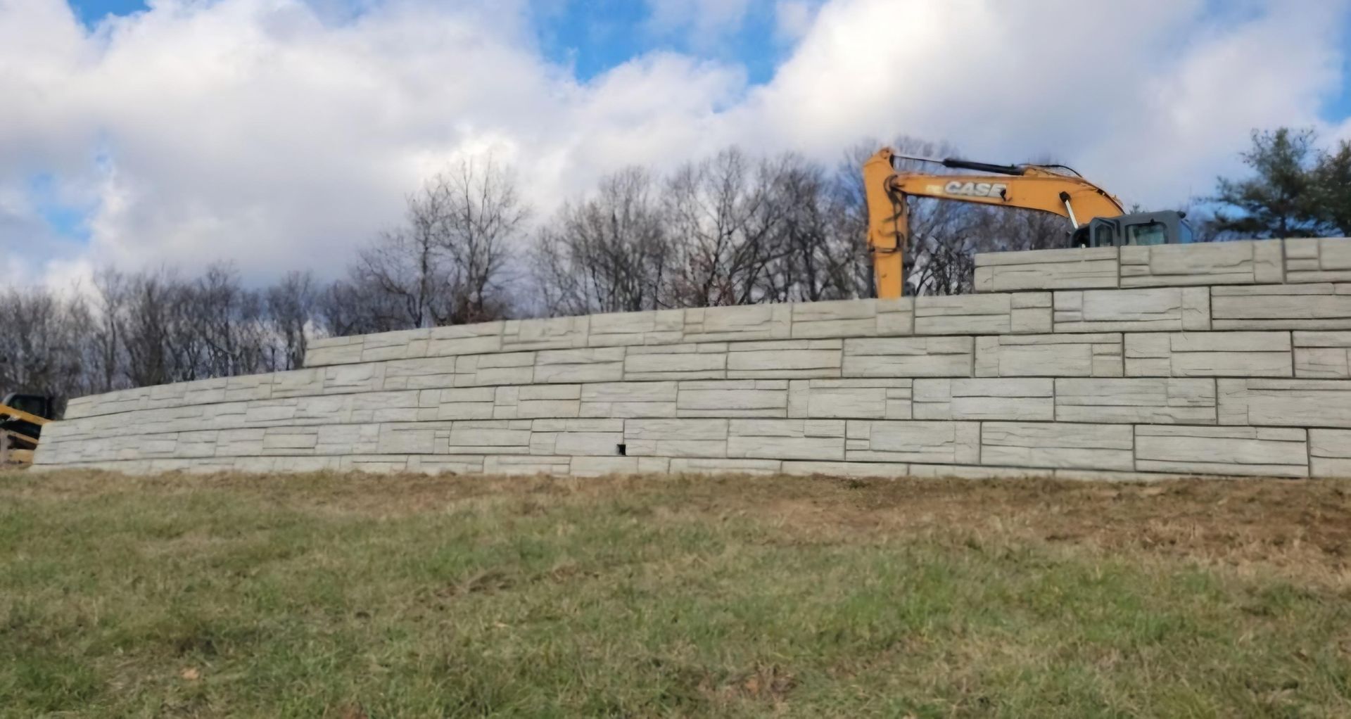 A large concrete wall is being built in a field with a bulldozer in the background.