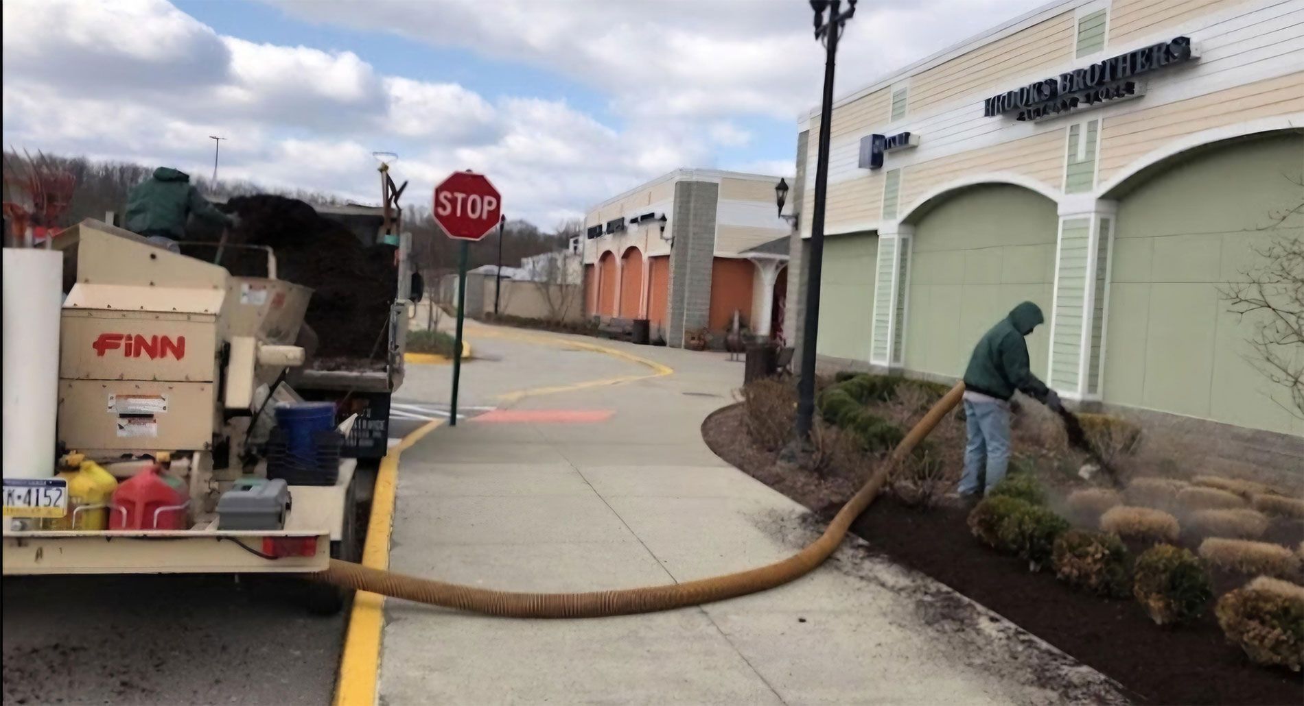 A man is cleaning a sidewalk with a finn truck in the background