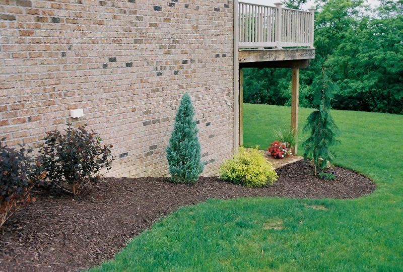 A brick house with a deck and a lush green lawn in front of it.
