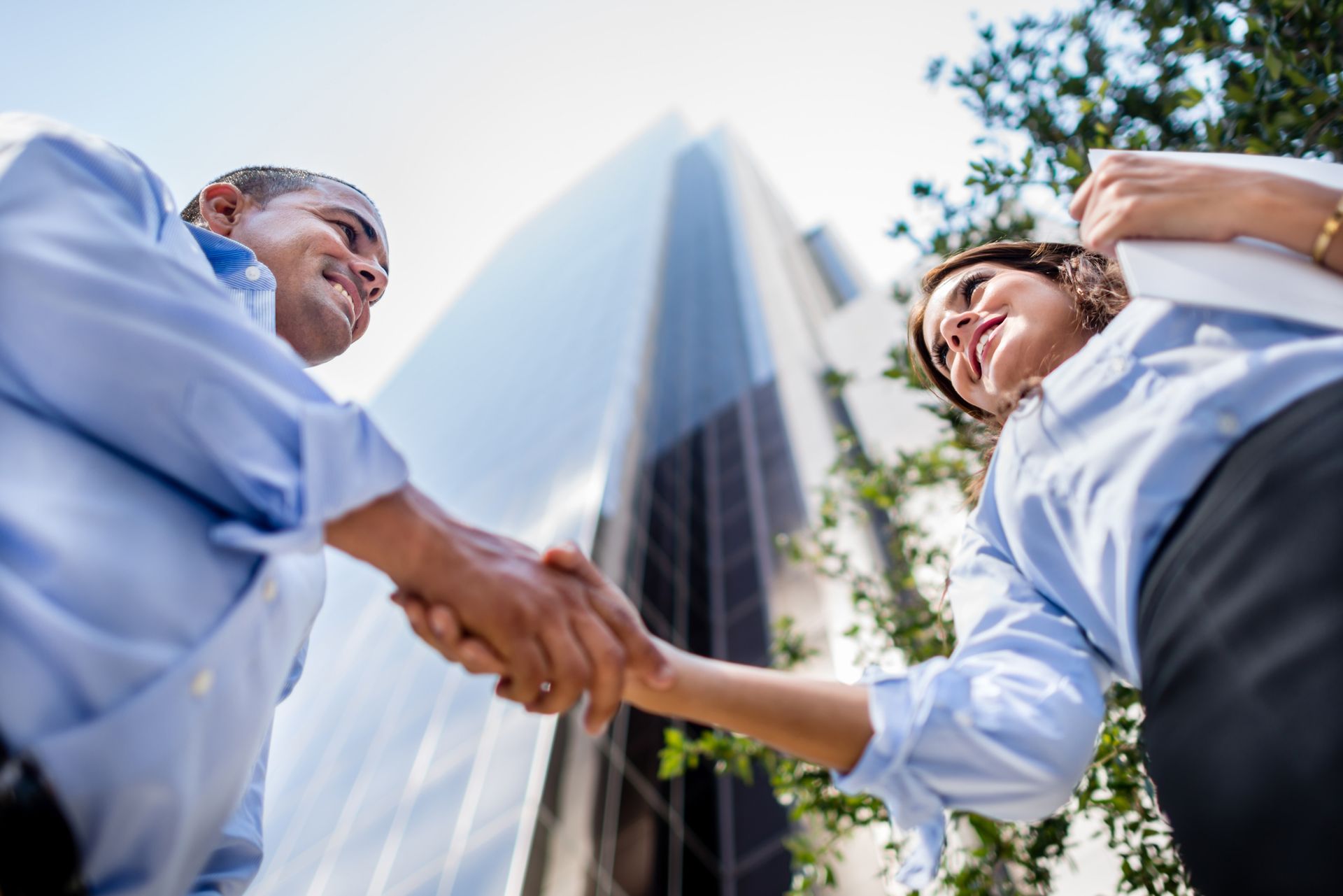 A man and a woman are shaking hands in front of a tall building.