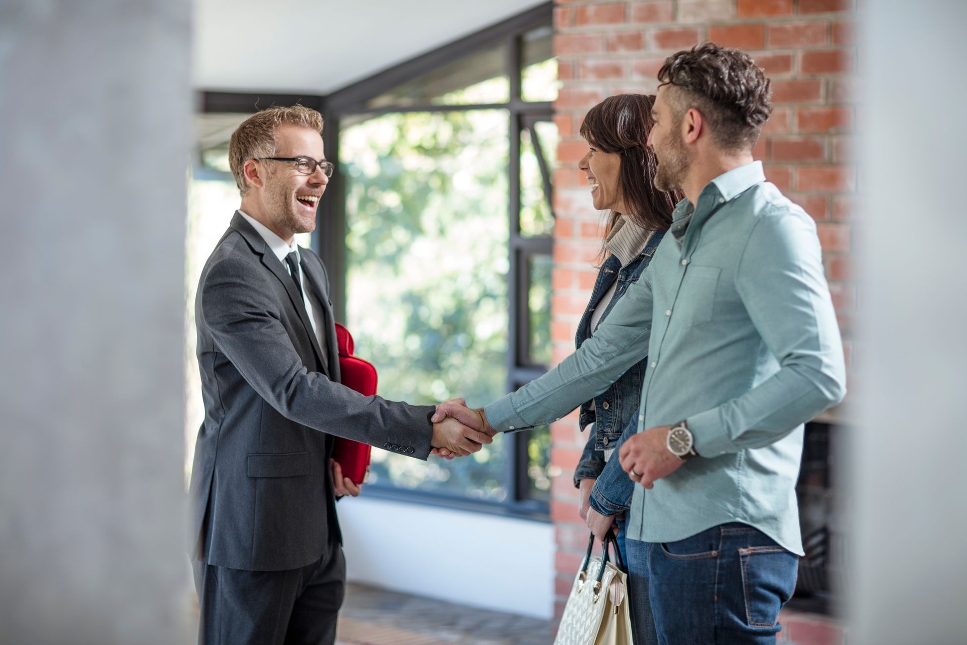 A man and woman are shaking hands with a real estate agent in a living room.