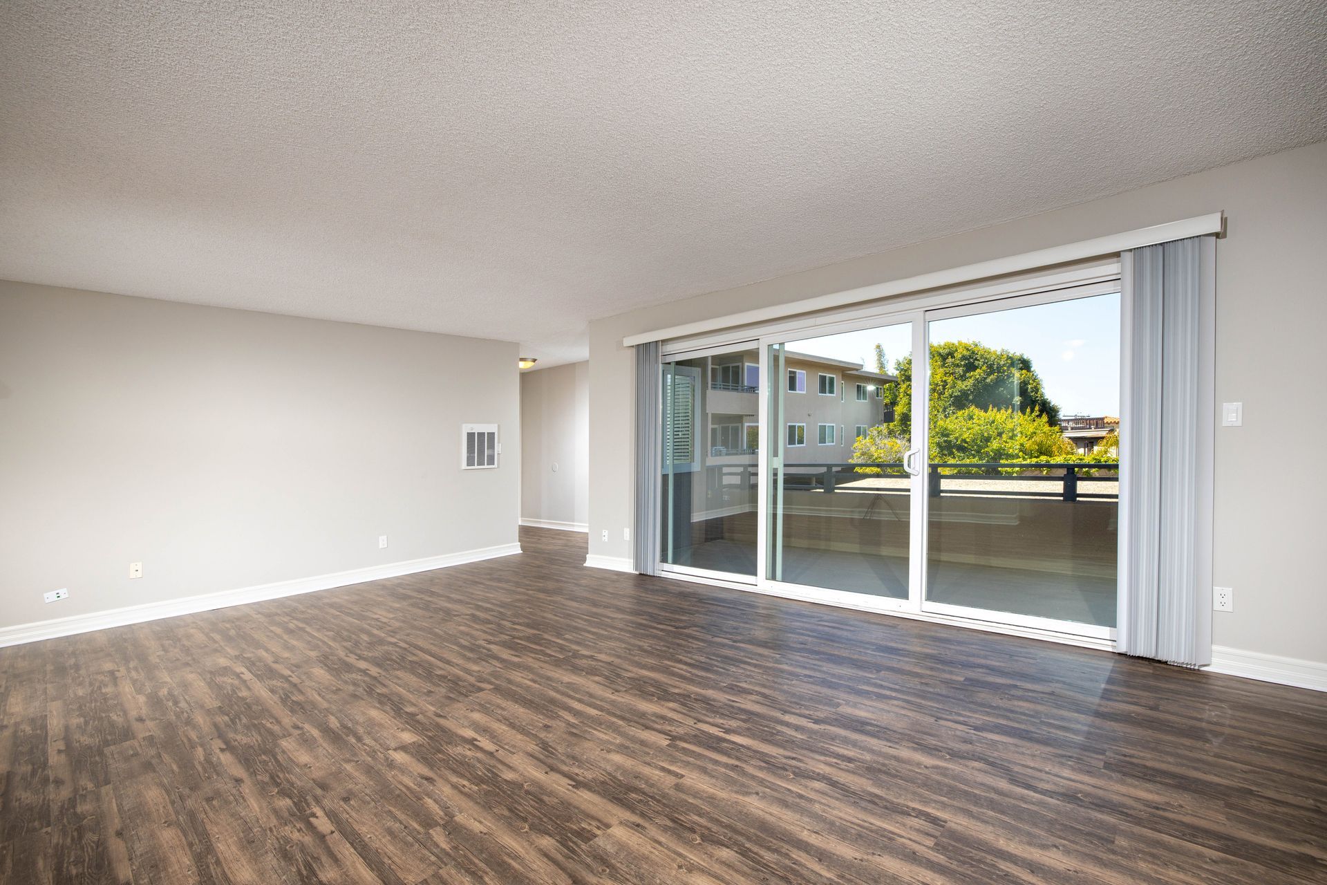 Empty modern living room with wood floors and sliding glass door to a balcony view