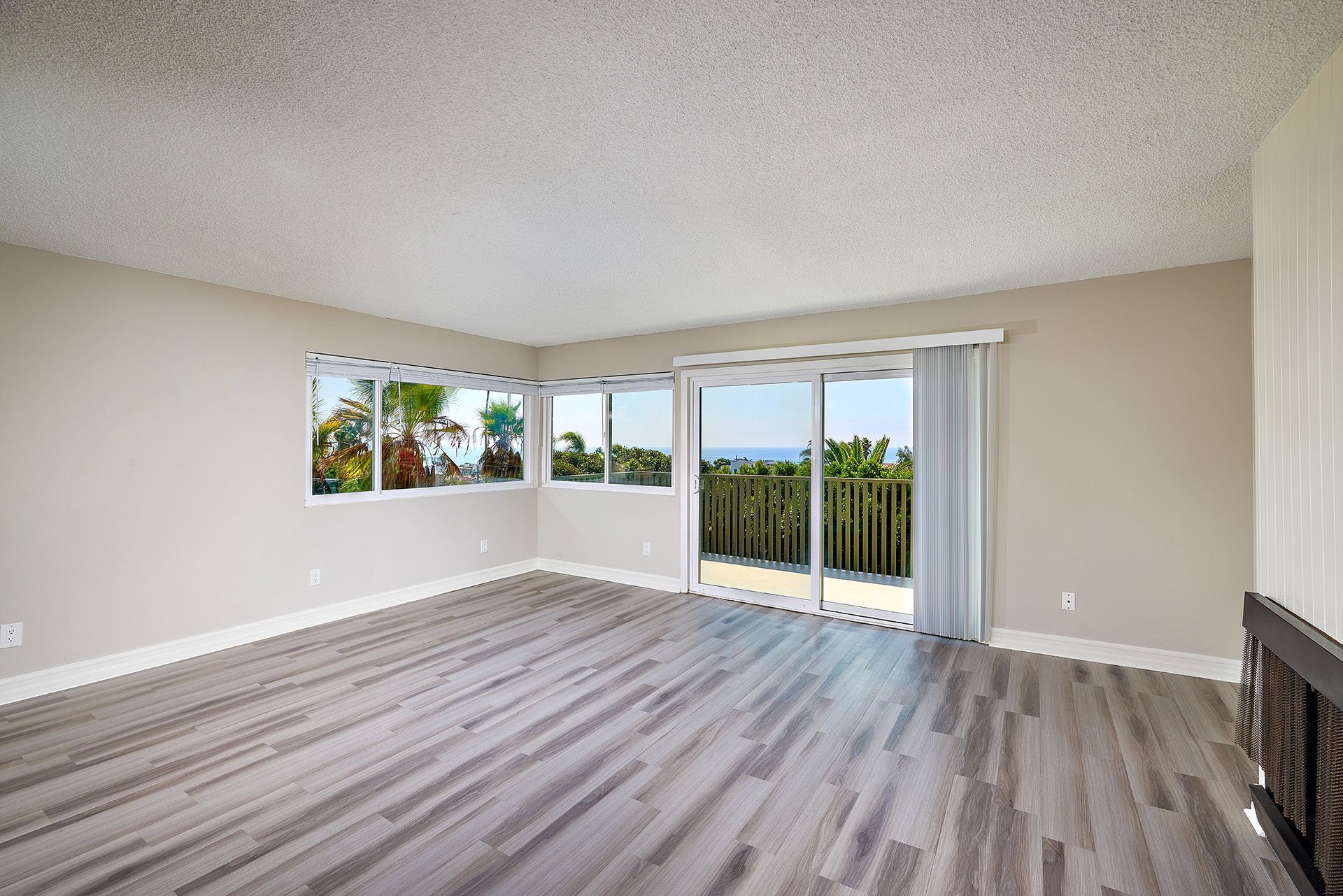 Empty living room with gray wood floors, large windows, and sliding glass doors to a balcony.