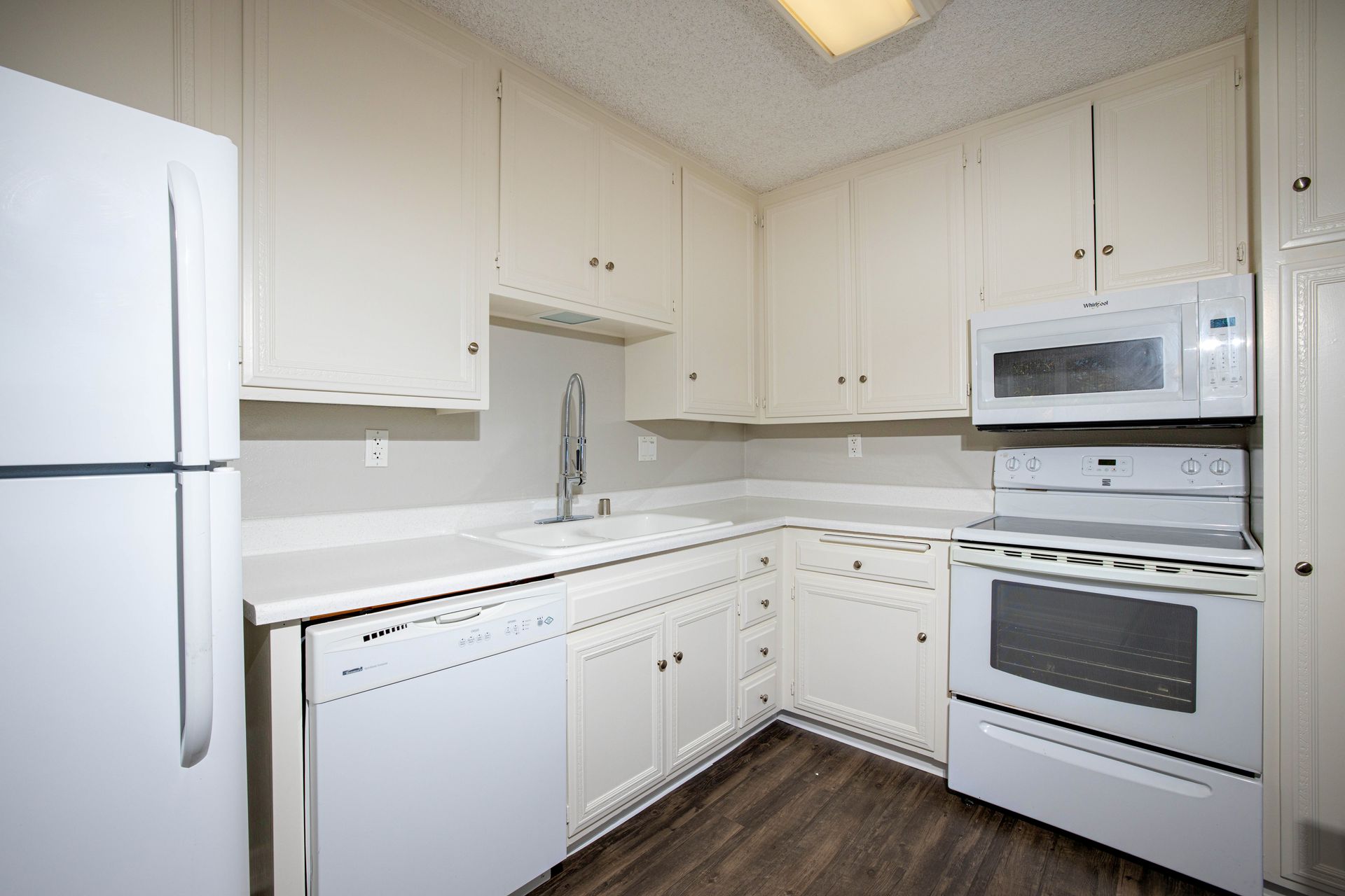 Bright white kitchen with refrigerator, stove, microwave, and corner cabinets
