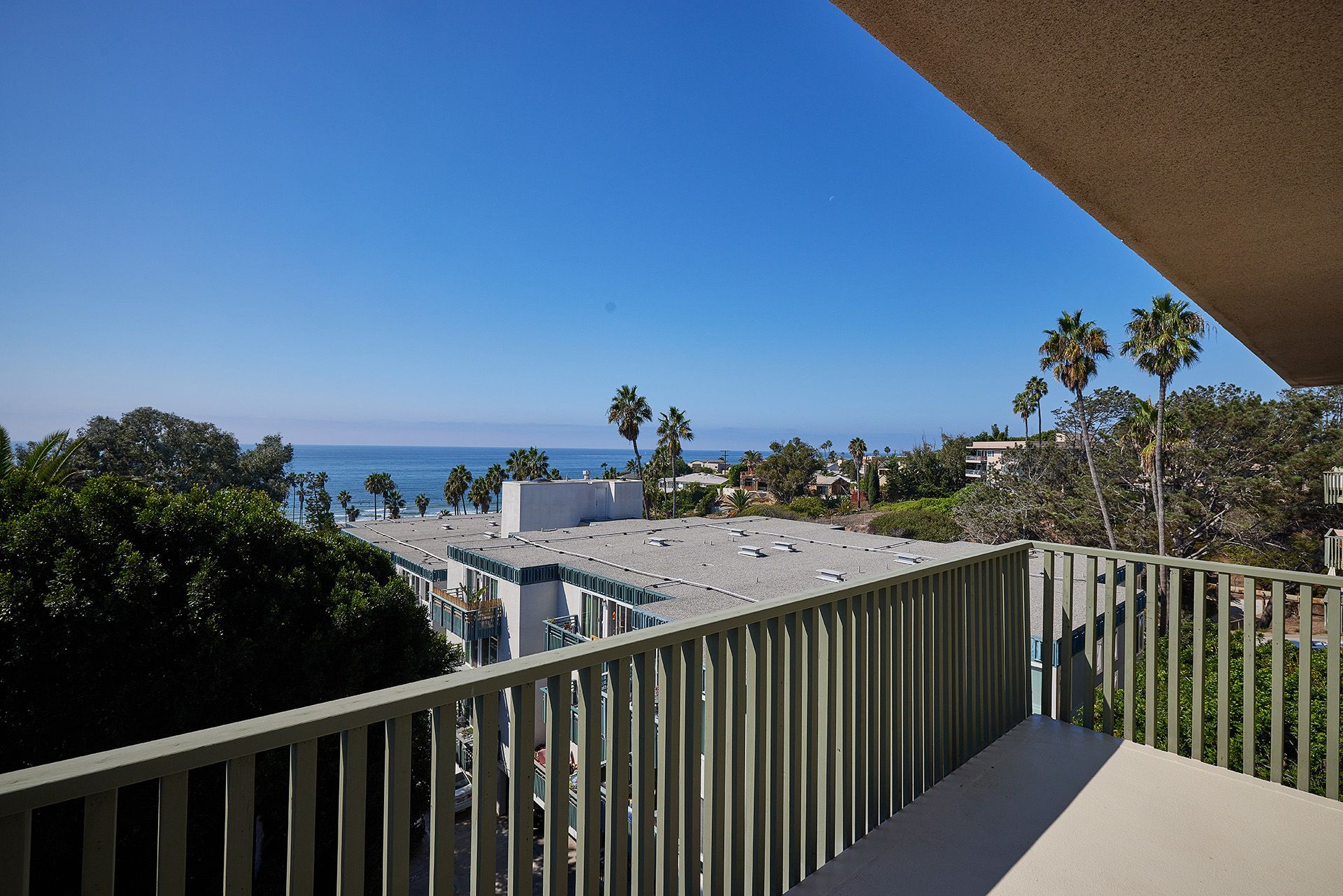 Balcony view of rooftops, palm trees, and the ocean under a clear blue sky