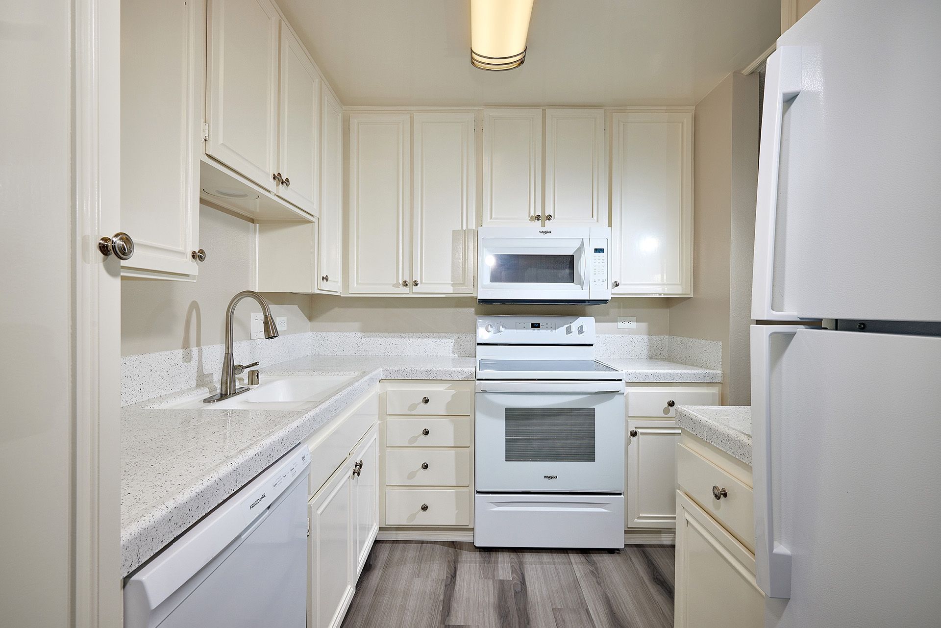White galley kitchen with white cabinets, countertop, stove, microwave, refrigerator, and gray floor.