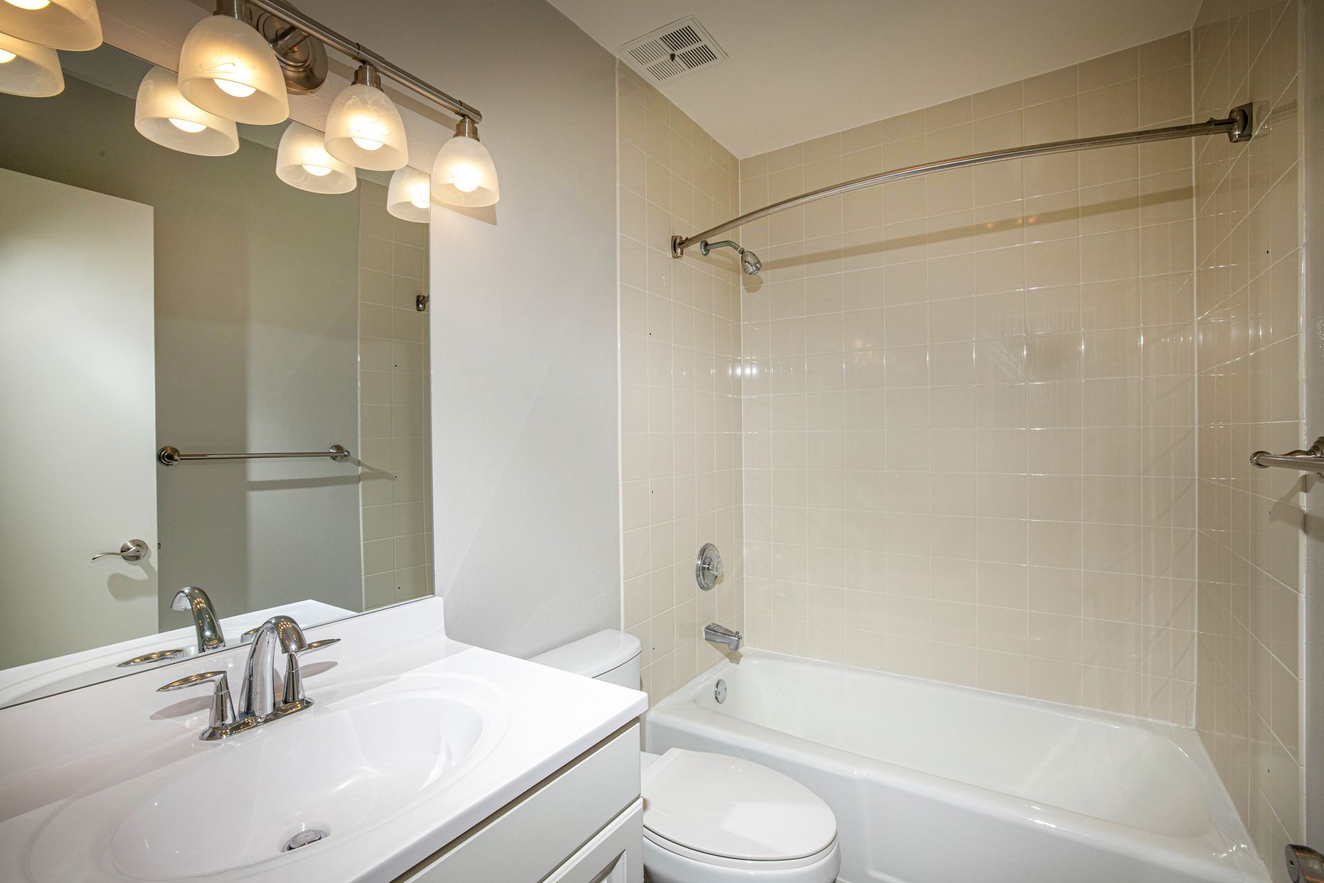 Bright white bathroom with vanity mirror, sink, toilet, and bathtub with shower curtain.