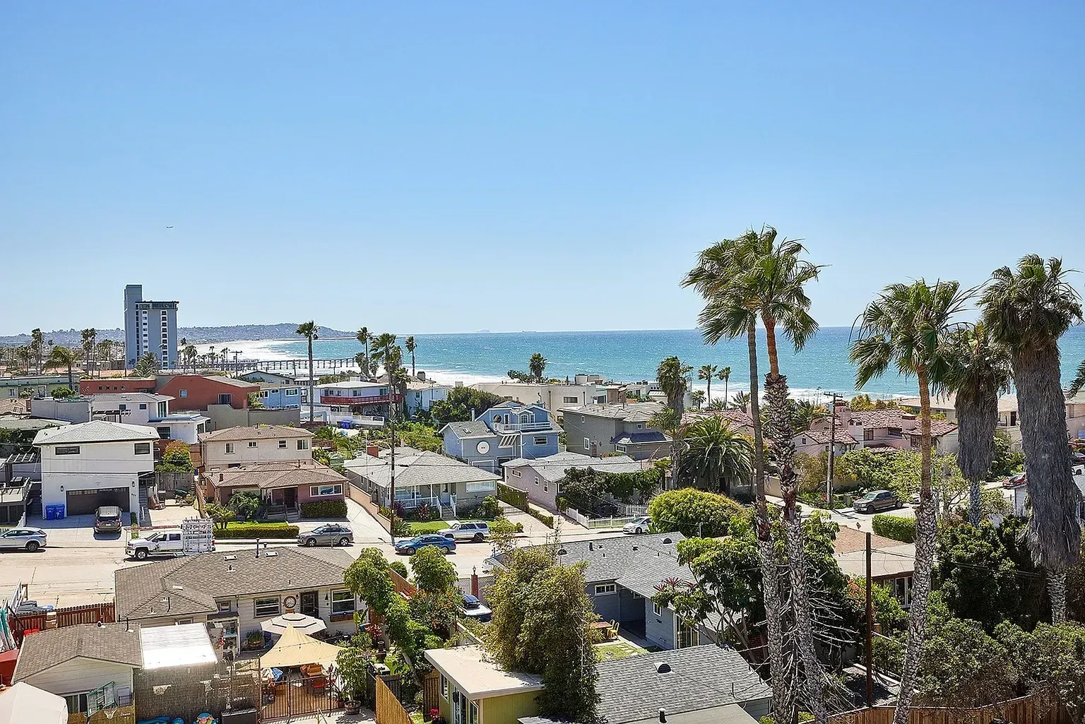 Coastal town rooftops and palm trees overlooking a blue ocean under a clear sky
