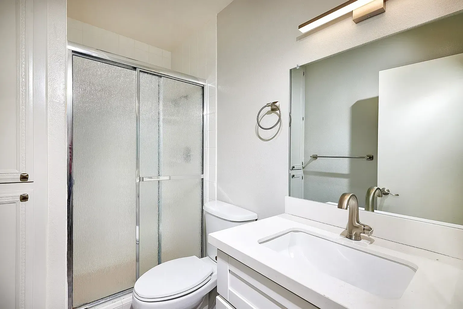 Bright bathroom with glass shower, toilet, and white vanity with mirror and gold faucet