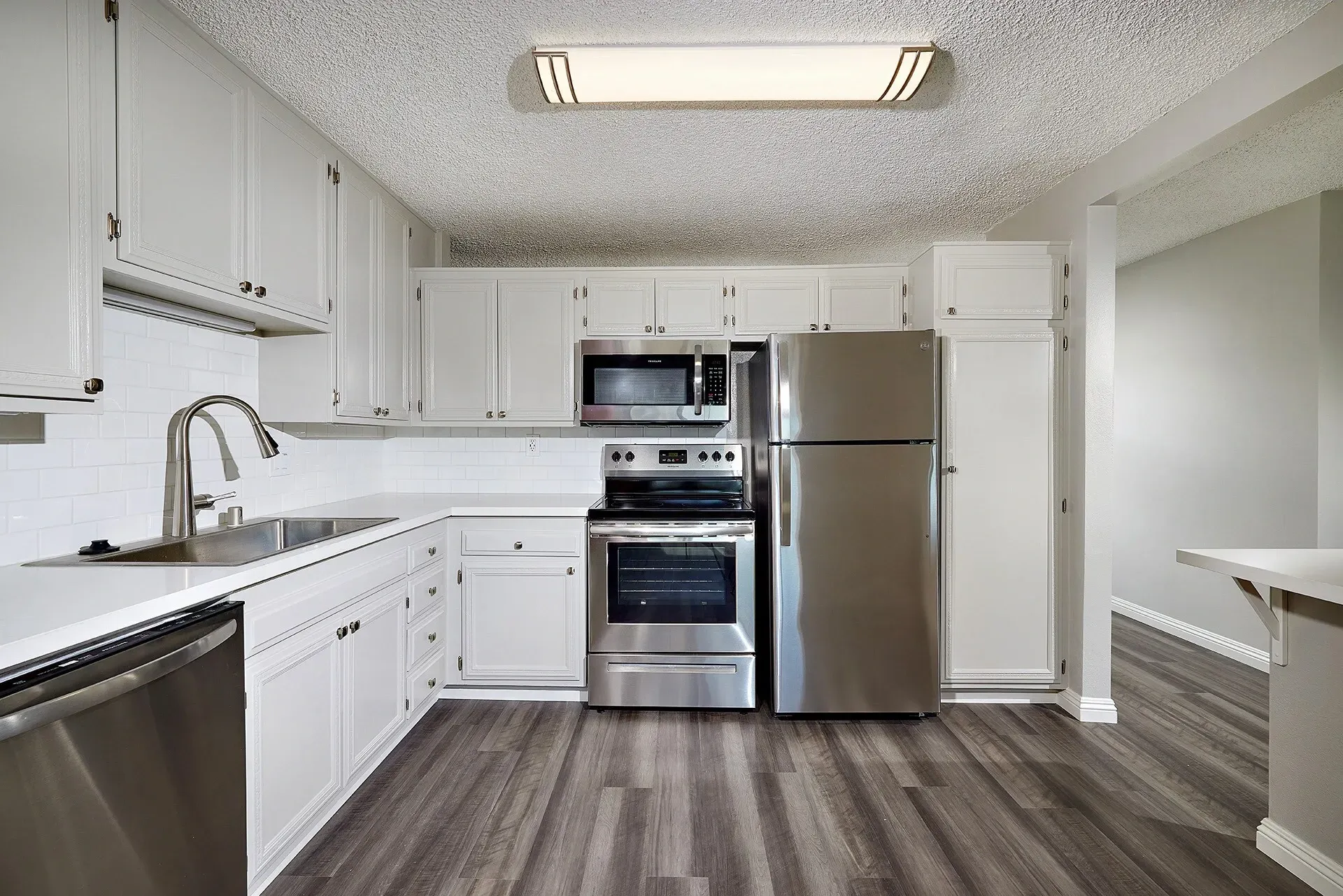 Bright modern kitchen with white cabinets, stainless steel appliances, and dark wood flooring