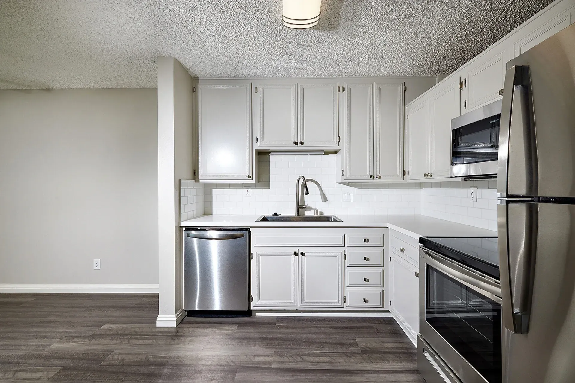 Empty modern kitchen with white cabinets, stainless steel appliances, and gray wood flooring.