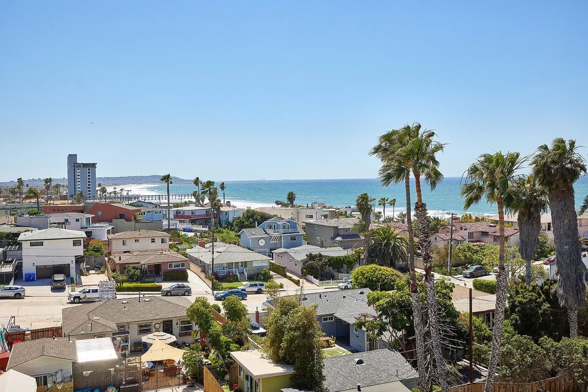 Coastal neighborhood with palm trees, rooftops, and the blue ocean under a clear sky