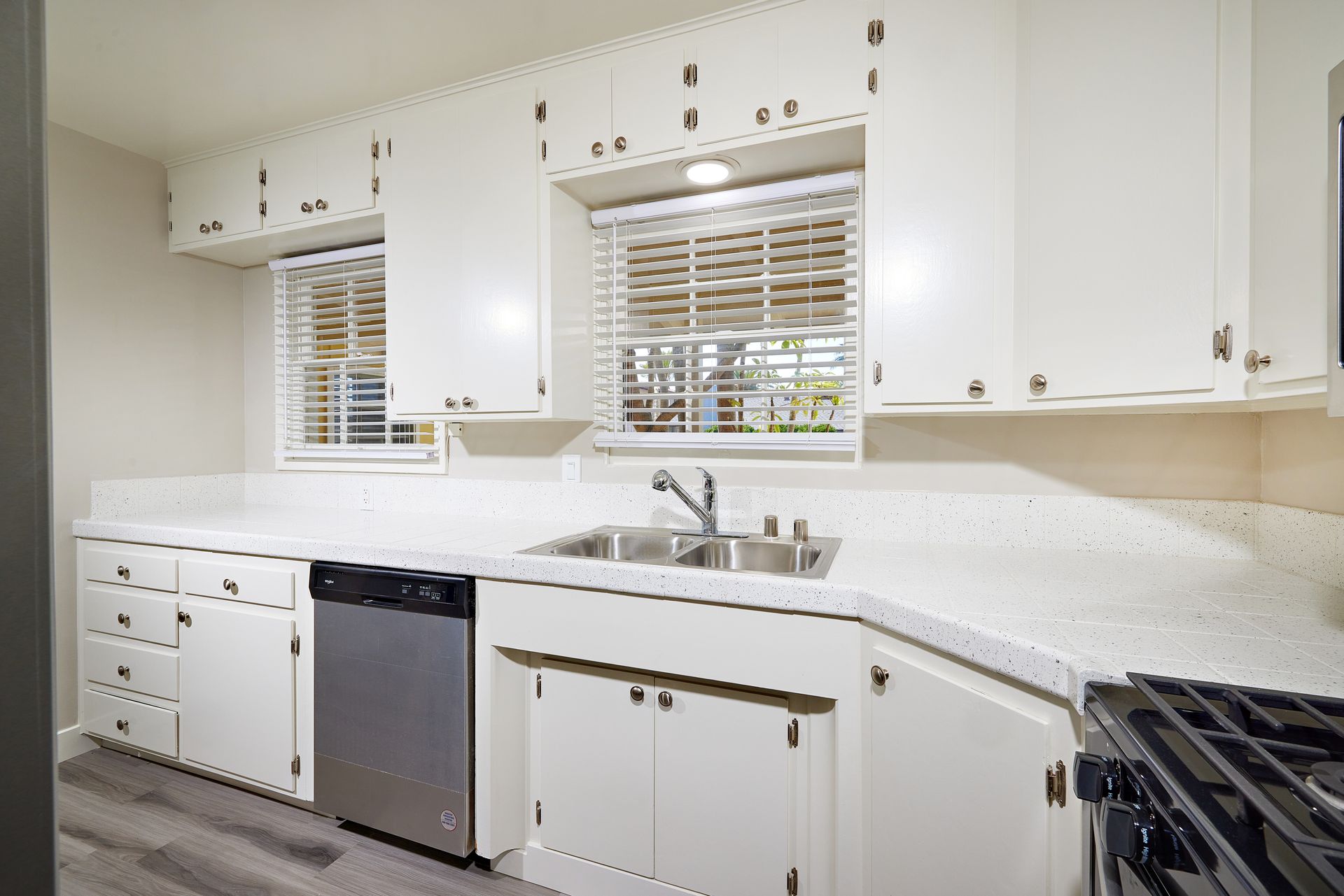 Bright white kitchen with cabinets, stainless dishwasher, sink under windows, and gas stove.