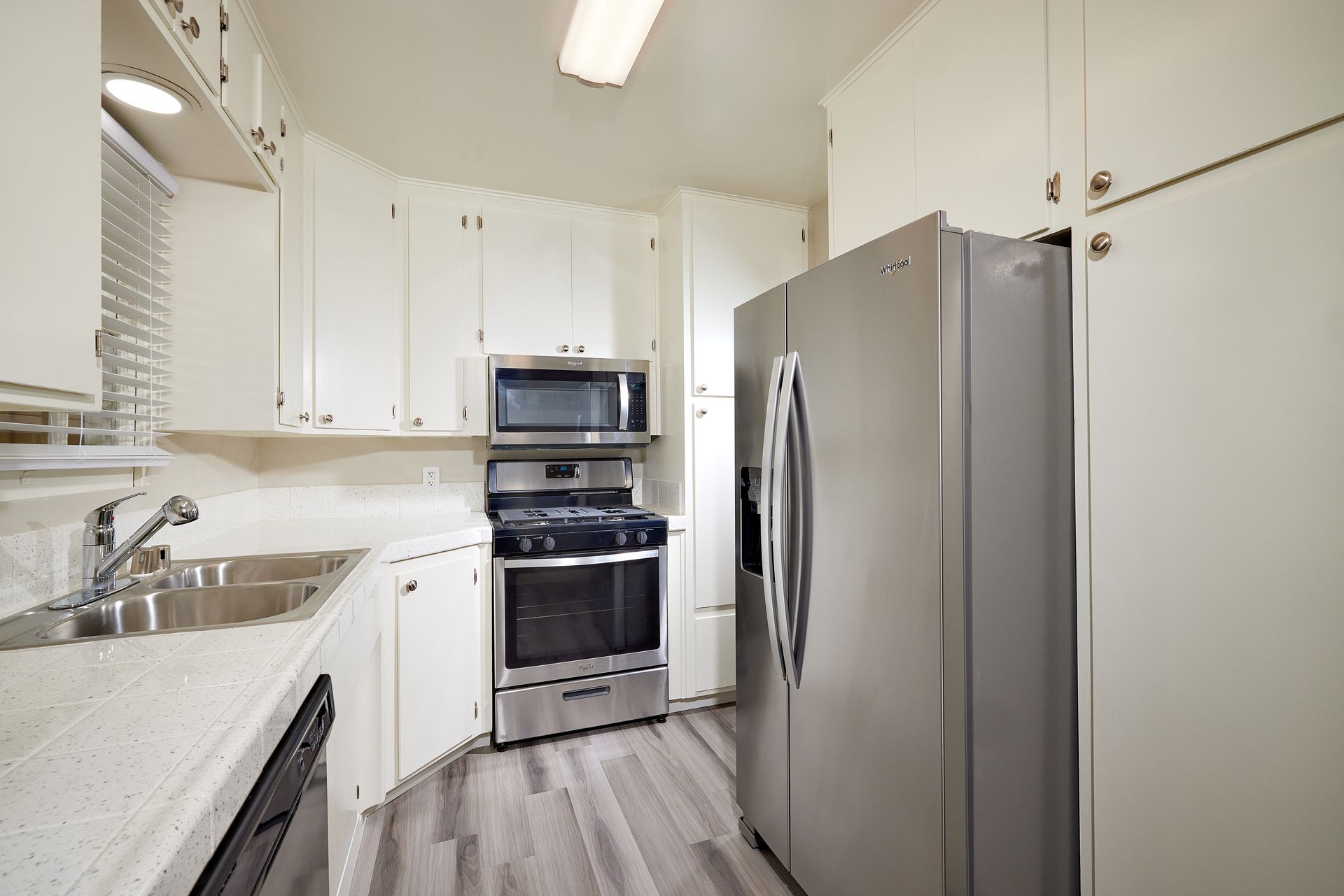 Bright white kitchen with stainless steel appliances, granite counters, and gray wood flooring