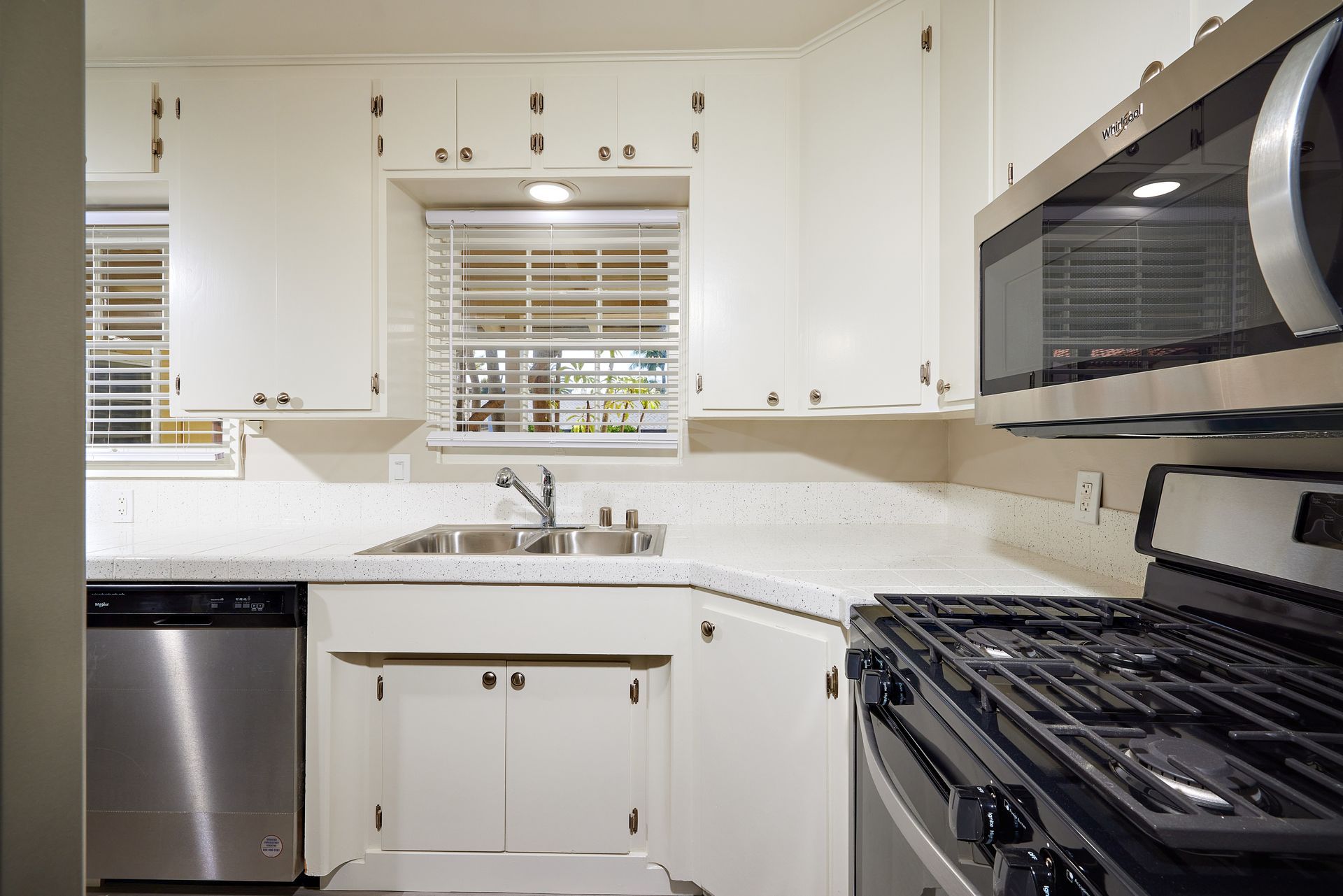 Bright white kitchen with stainless steel appliances, window above sink, and black gas stove.