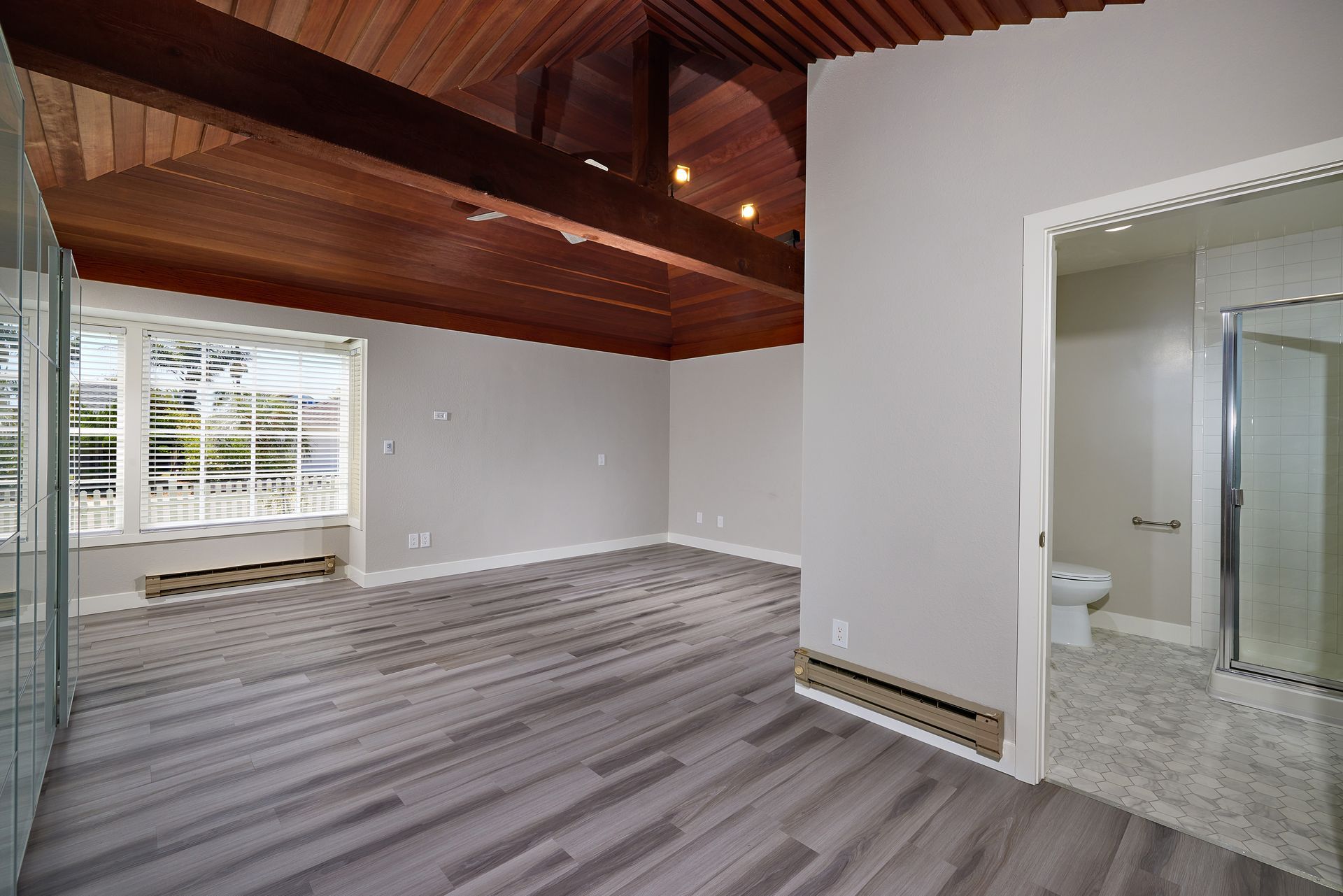 Empty modern room with wood ceiling, gray carpet, large windows, and attached bathroom view