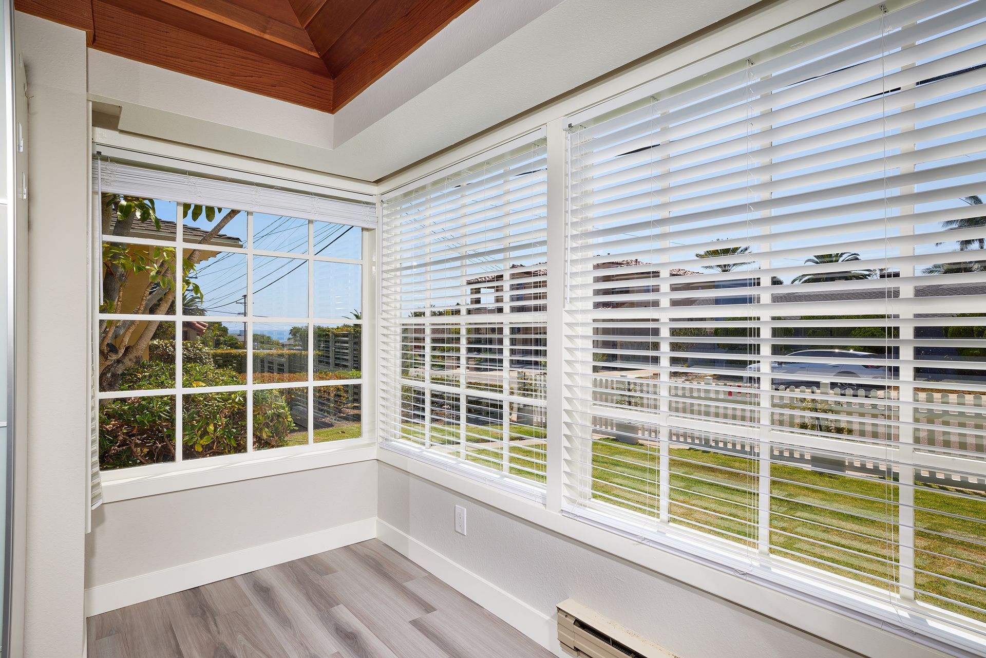 Bright sunroom with white blinds, large windows, and a view of a grassy outdoor area.