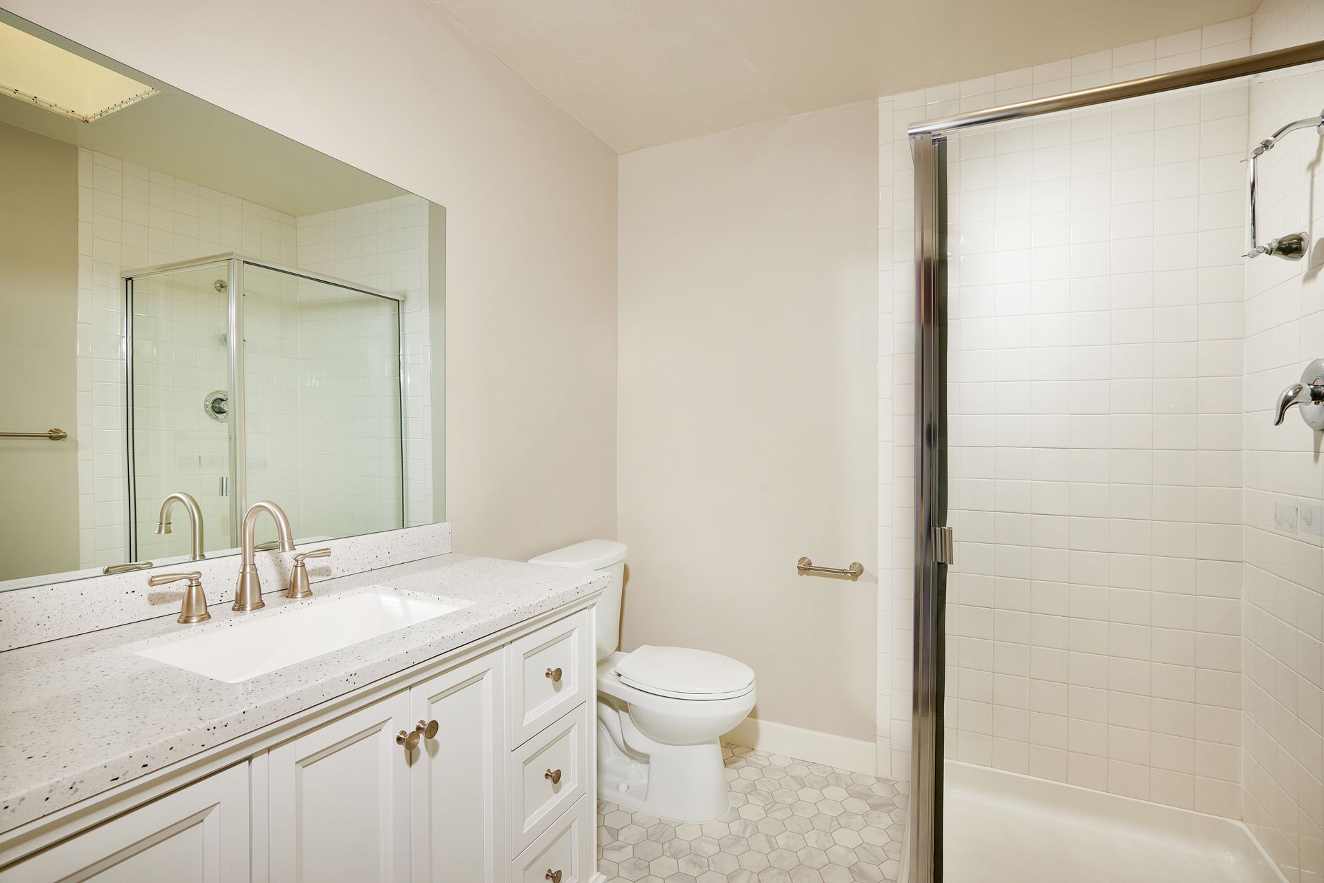 Bright bathroom with double sink, toilet, large mirror, and glass shower stall.