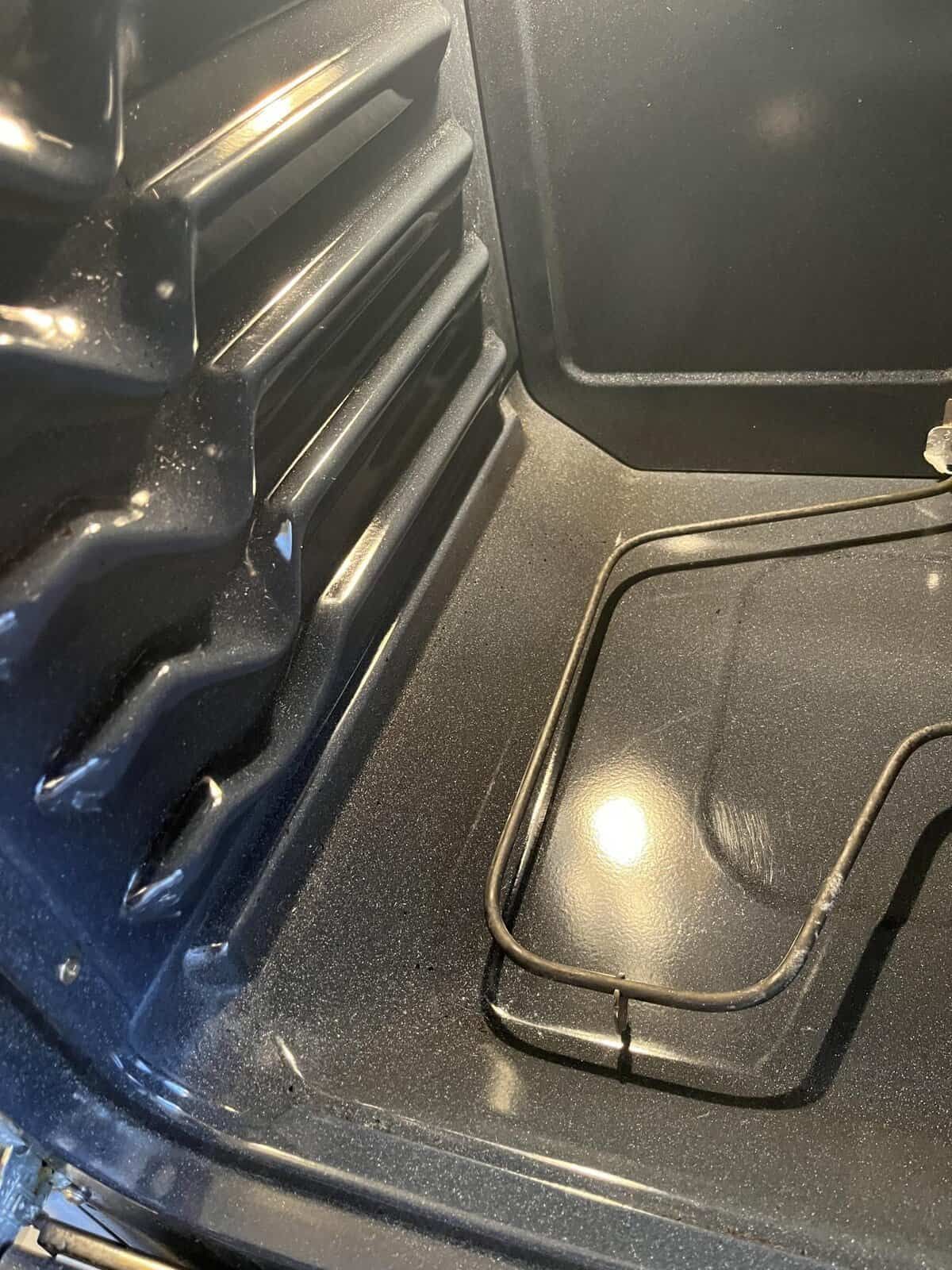 Interior of a dark oven with a heating element and a grimy surface.