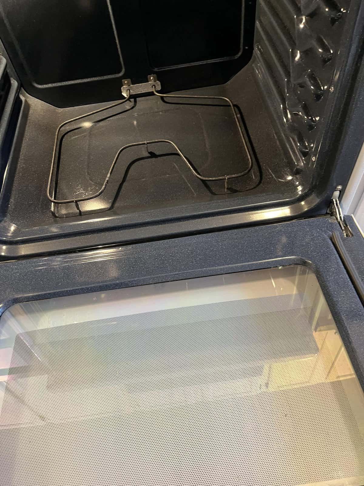 Open oven interior with wire rack, dark surfaces, and patterned glass door.