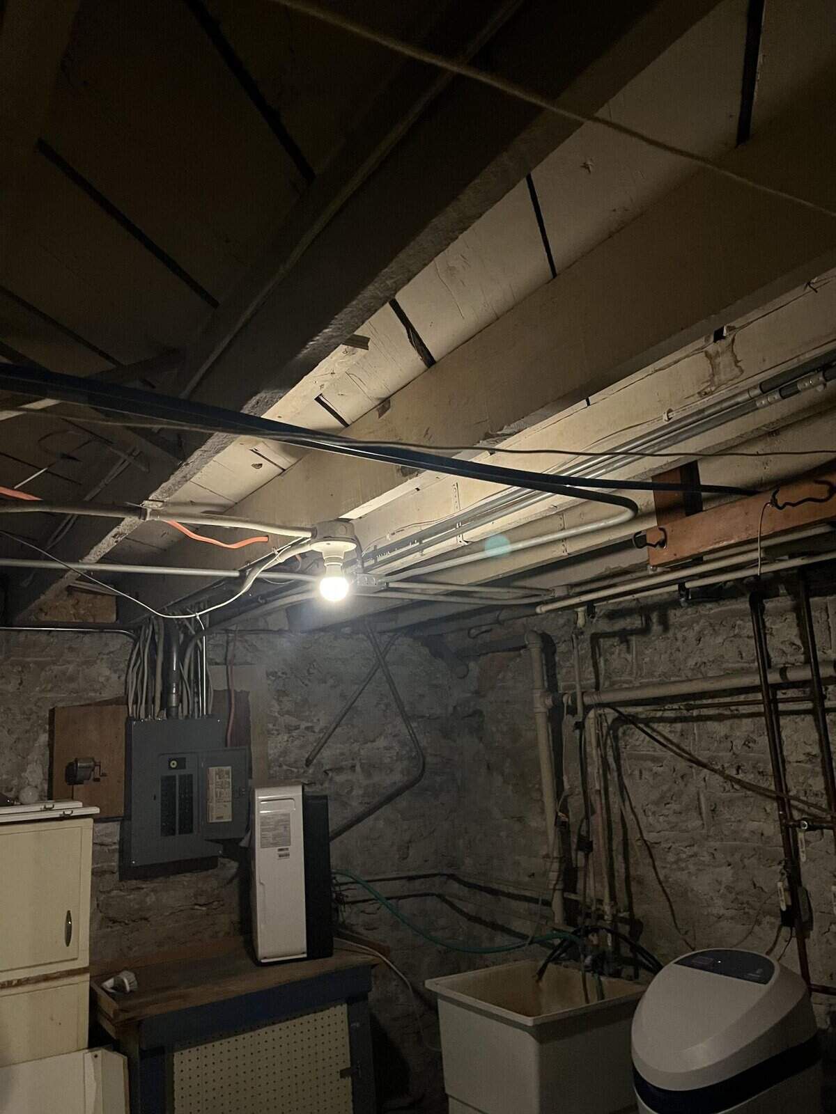 Basement interior with exposed beams, pipes, electrical panel, and appliances.