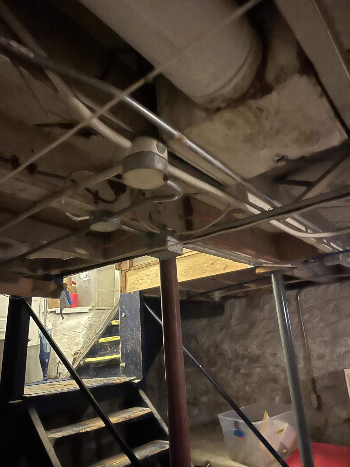 Basement ceiling with pipes, electrical wiring, and a smoke detector. Metal stairs lead upward.