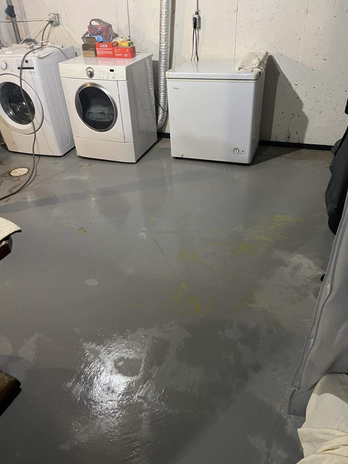 Laundry room with gray painted floor, washing machines, and a freezer. The floor appears wet.