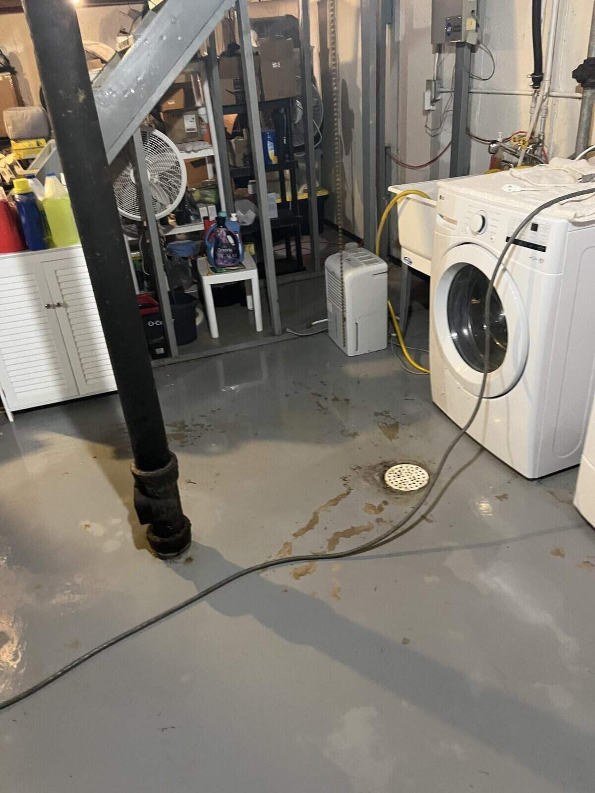 Basement with a washing machine, drain, and a black pipe. The floor is light gray.