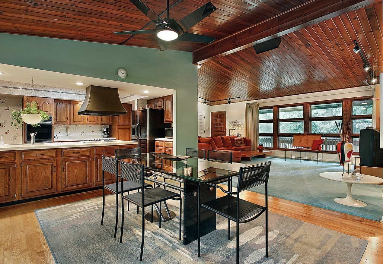 Open-concept living space with kitchen, dining area, and living room. Wooden ceiling, teal walls, and furniture.