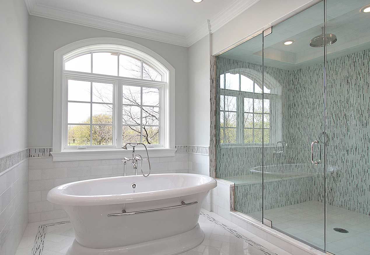 Elegant white bathroom with a freestanding tub under an arched window, a glass shower.