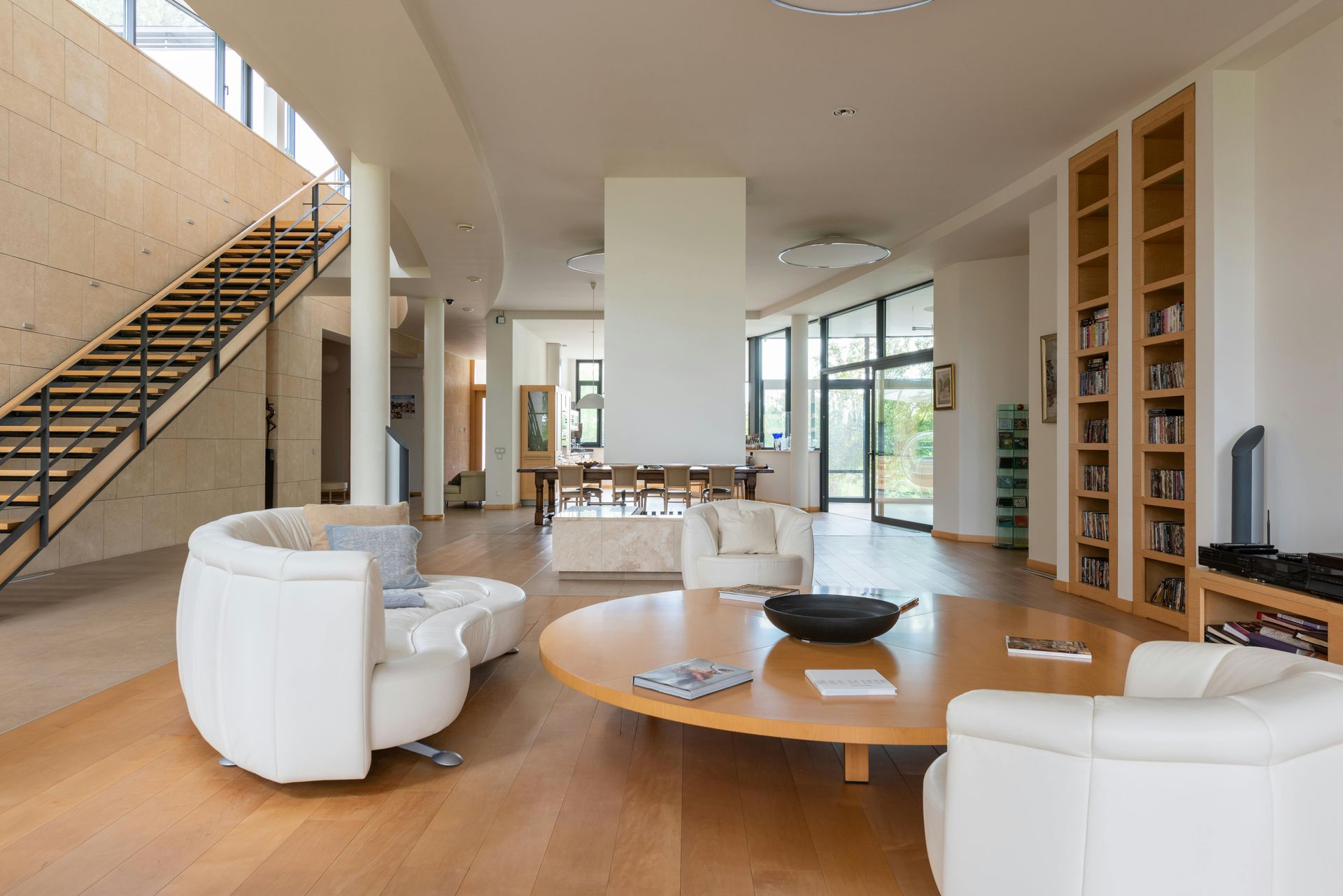 Spacious living room with white seating, a large wooden table, and a staircase.