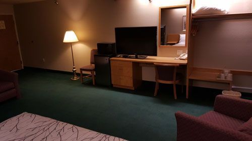 A hotel room with a couch , chair , desk and television.
