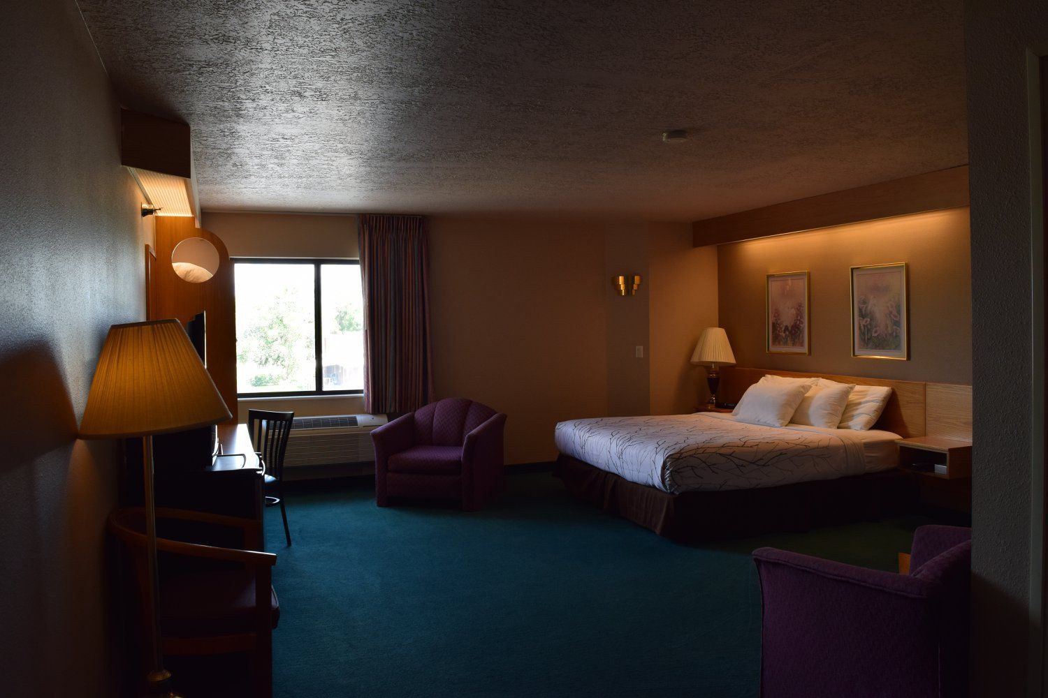 A hotel room with a bed , chair , desk and lamp