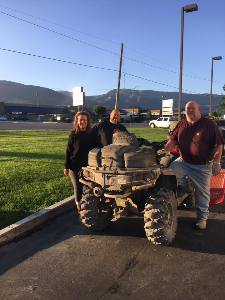 Two men and a woman are standing next to an atv