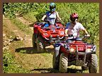 A man and a woman are riding four wheelers down a dirt road.