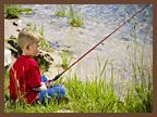 A young boy is sitting in the grass holding a fishing rod.