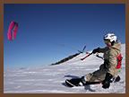 A person is flying a kite while snowboarding in the snow.