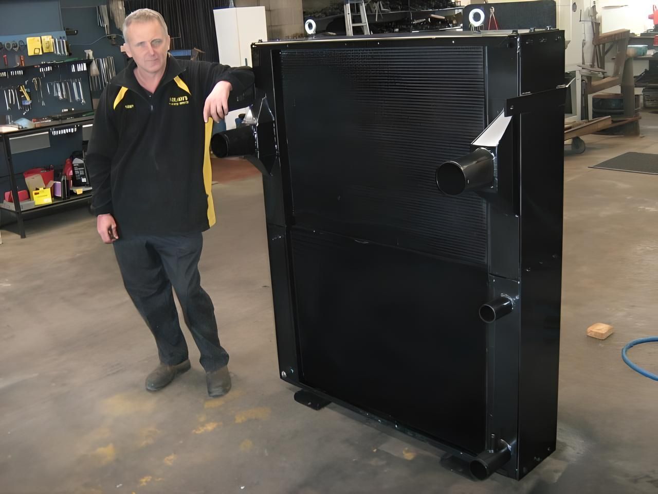 Man Stands Next to a Large, Black Intercooler in a Workshop Setting — Neilsen's Radiator Service in Toowoomba City, QLD
