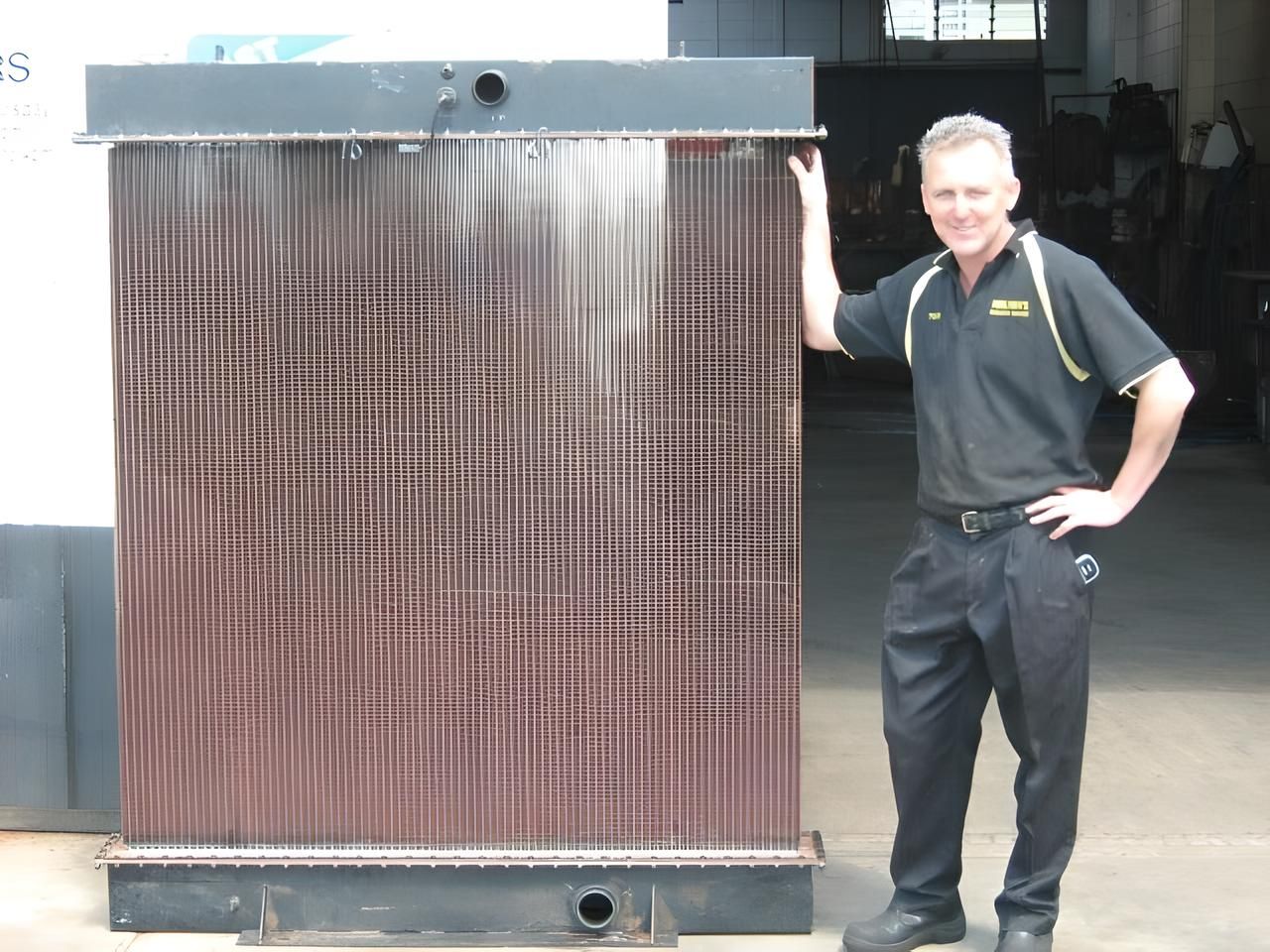 A Man is Standing Next to a Large Radiator — Neilsen's Radiator Service in Toowoomba, QLD