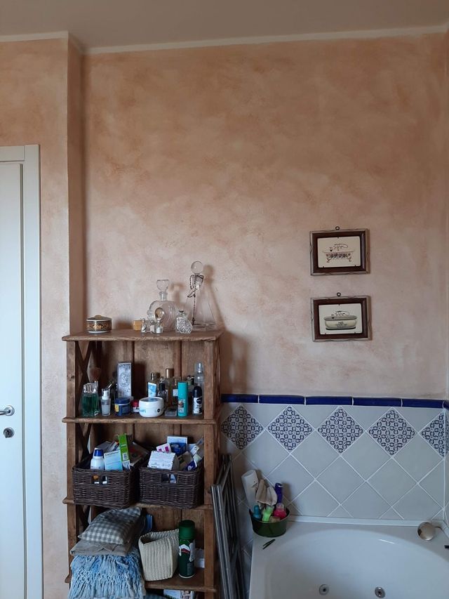 Un bagno con pareti arancioni testurizzate, una mensola in legno con articoli da toeletta e dettagli piastrellati blu e bianchi.